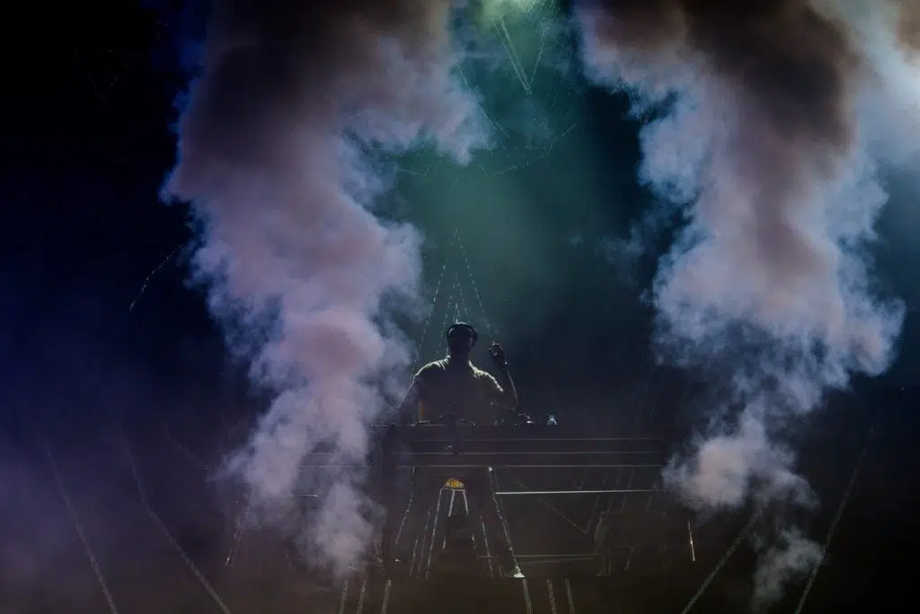 a DJ on a stage with smoke behind him